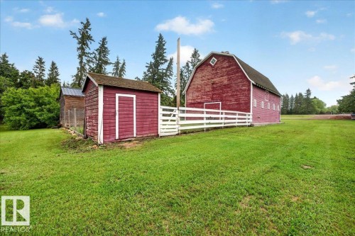 Expansive green lawn featuring a red barn, a red shed, a white fence, mature trees, and a distant wooded area - 572004 Highway 857, Rural Two Hills County, AB 