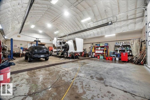 Spacious garage featuring a high arched ceiling, multiple overhead light fixtures, and a vehicle lift - 572004 Highway 857, Rural Two Hills County, AB 