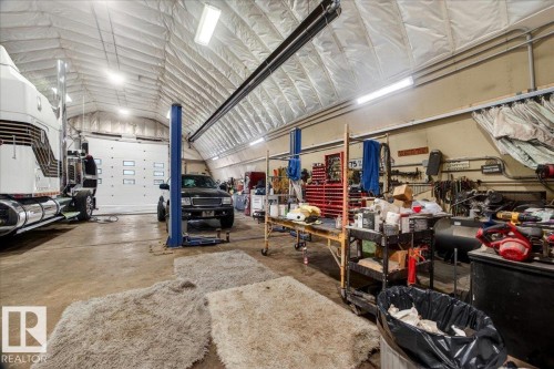 Spacious, high-ceiling structure featuring a large overhead door, an automotive lift, and ample workspace - 572004 Highway 857, Rural Two Hills County, AB 