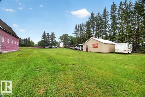 Expansive green lawn with a red-sided barn and a tan-sided outbuilding - 572004 Highway 857, Rural Two Hills County, AB 