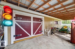 Utility building featuring a red barn-style door with white trim, a concrete floor, and an exposed wood beam ceiling with a metal roof - 