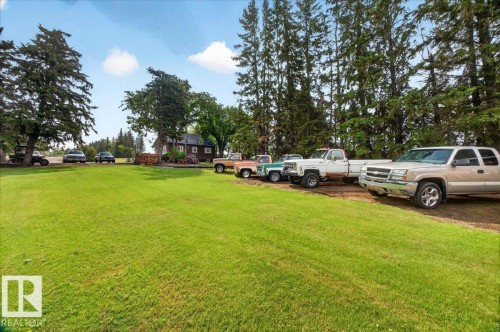 Expansive green lawn surrounded by mature trees, featuring a brown-sided structure with a dark roof in the background - 572004 Highway 857, Rural Two Hills County, AB 