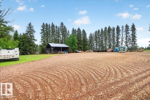 Expansive gravel lot featuring a large open-sided shed with a metal roof, surrounded by mature evergreen trees - 572004 Highway 857, Rural Two Hills County, AB 