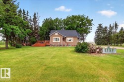 Expansive green lawn surrounding a charming residence with a dark shingle roof, light-colored trim, and a raised wooden deck - 