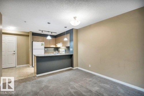 Open-concept living space featuring a kitchen with light wood-finish cabinetry, a white refrigerator, and a breakfast bar with pendant lighting - 116 630 Mcallister Loop, Edmonton, AB 