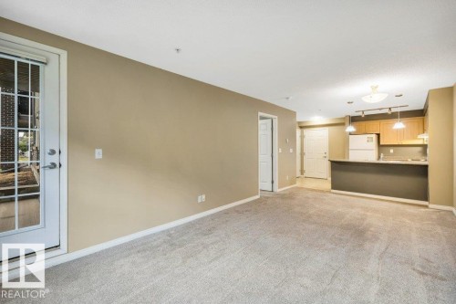 Spacious living area featuring neutral carpeting and a glass-paned door - 116 630 Mcallister Loop, Edmonton, AB 