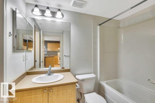 Bathroom featuring a wood-finish vanity with a beige countertop, a single basin sink, and a large mirror - 116 630 Mcallister Loop, Edmonton, AB 