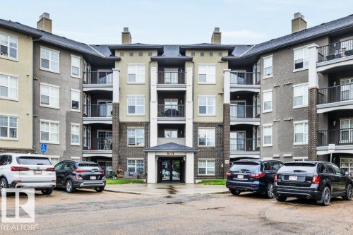Modern multi-story residential building featuring a central entrance canopy, multiple private balconies with dark railings, and a facade combining brick-finish and stucco elements - 116 630 Mcallister Loop, Edmonton, AB 