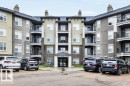 Modern multi-story residential building featuring a central entrance canopy, multiple private balconies with dark railings, and a facade combining brick-finish and stucco elements - 116 630 Mcallister Loop, Edmonton, AB 