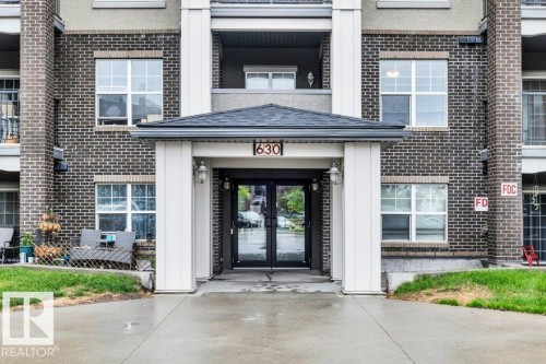 Building exterior featuring a covered entryway with a pitched roof, dark brick facade, and multiple windows - 116 630 Mcallister Loop, Edmonton, AB 