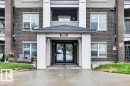 Building exterior featuring a covered entryway with a pitched roof, dark brick facade, and multiple windows - 116 630 Mcallister Loop, Edmonton, AB 