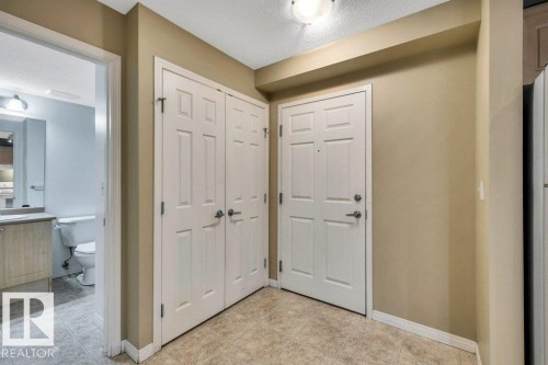 Entry area featuring a solid panel front door with brushed nickel hardware, neutral wall paint, and textured ceiling - 116 630 Mcallister Loop, Edmonton, AB 