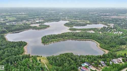 Expansive aerial landscape featuring a large lake surrounded by dense green forestry, with residential structures visible along the distant shoreline - 337 Smith Crescent, Rural Parkland County, AB 