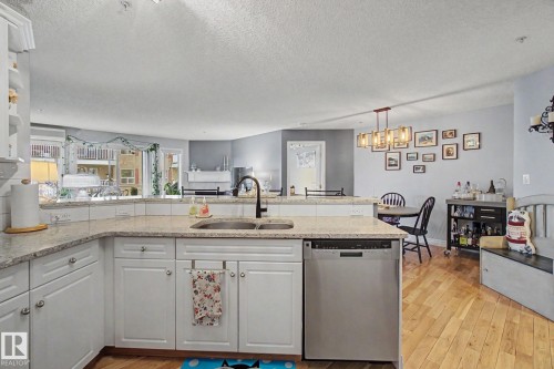 Contemporary kitchen with white cabinetry, light-toned countertops, and a stainless steel dishwasher - 308 10933 124 Street, Edmonton, AB 