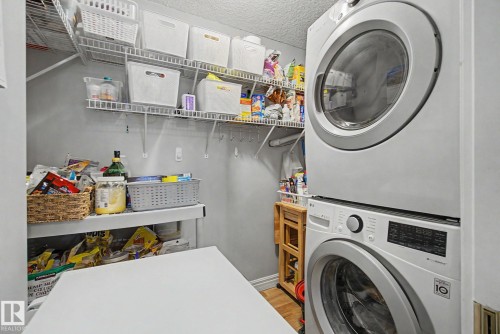 Laundry area featuring a stacked washer and dryer unit, wire shelving, and a folding surface - 308 10933 124 Street, Edmonton, AB 