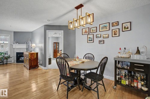 Dining area featuring hardwood flooring, a contemporary chandelier, a painted accent wall, and a fireplace with a mantel in an adjoining space - 308 10933 124 Street, Edmonton, AB 