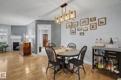 Dining area featuring hardwood flooring, a contemporary chandelier, a painted accent wall, and a fireplace with a mantel in an adjoining space - 