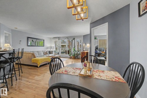 Open-concept living space featuring wood-finish flooring, a contemporary chandelier, and a breakfast bar with seating - 308 10933 124 Street, Edmonton, AB 
