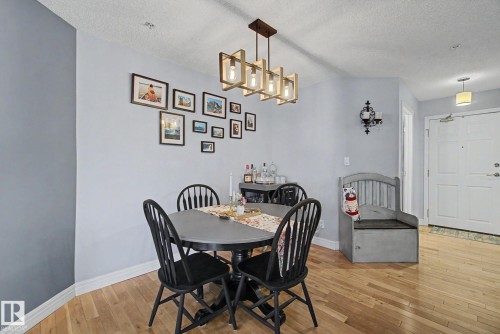 Open dining area featuring wood-finish flooring, a contemporary linear chandelier, and light-toned walls - 308 10933 124 Street, Edmonton, AB 