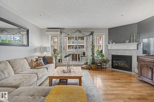 Living area featuring wood-finish flooring and a corner fireplace with a white mantel and light-toned tile surround - 308 10933 124 Street, Edmonton, AB 