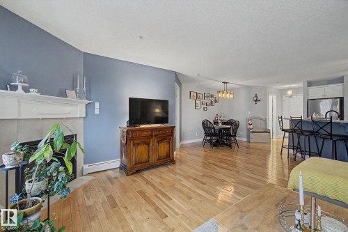 Open-concept living space featuring wood-finish flooring, a fireplace with a white mantel, and a dining area with a modern chandelier - 308 10933 124 Street, Edmonton, AB 
