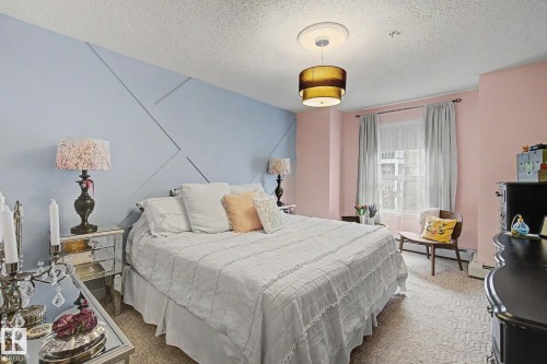 Bedroom featuring a textured accent wall, window with curtains, and a ceiling-mounted light fixture - 308 10933 124 Street, Edmonton, AB 
