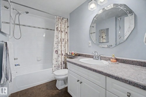 Bathroom featuring a white vanity with an integrated sink, a laminate countertop, and a decorative octagonal mirror - 308 10933 124 Street, Edmonton, AB 