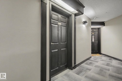 Hallway featuring grey patterned carpet tile flooring, light neutral wall paint, and dark paneled doors with matching trim - 308 10933 124 Street, Edmonton, AB 