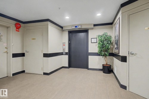 Contemporary hallway featuring light-toned flooring, recessed lighting, and a dark-toned elevator door - 308 10933 124 Street, Edmonton, AB 