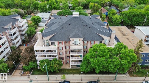 Multi-story residential building featuring a dark shingle roof, multiple private balconies with white railings, and a light-colored facade with red shutters - 308 10933 124 Street, Edmonton, AB 