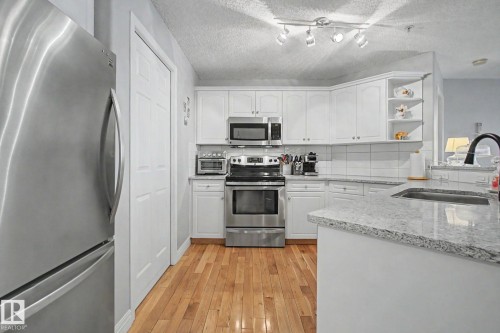 Kitchen featuring white cabinetry, stainless steel appliances, speckled countertops, a tile backsplash, and wood-finish flooring - 308 10933 124 Street, Edmonton, AB 