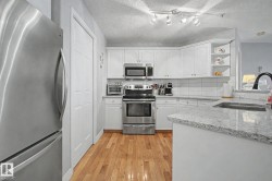 Kitchen featuring white cabinetry, stainless steel appliances, speckled countertops, a tile backsplash, and wood-finish flooring - 