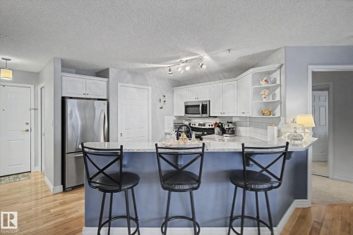 Kitchen featuring white cabinetry, stainless steel appliances, a white subway tile backsplash, light-toned countertops, and a breakfast bar with seating - 308 10933 124 Street, Edmonton, AB 