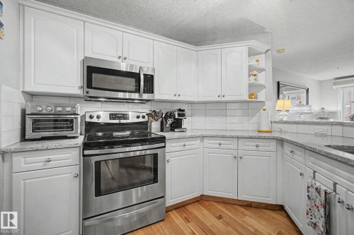 Kitchen featuring white cabinetry, light-toned countertops, a full suite of stainless steel appliances, and wood-finish flooring - 308 10933 124 Street, Edmonton, AB 