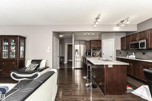 Open-concept kitchen featuring dark wood cabinetry, stainless steel appliances, a center island with a sink, track lighting, and wood-finish flooring - 115 57 Street, Edmonton, AB 