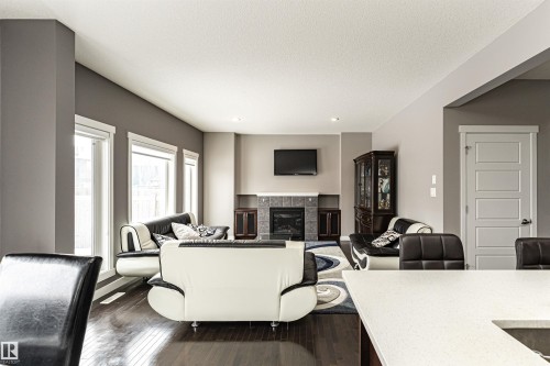 Spacious living area featuring dark wood-finish flooring, a contemporary fireplace with a tiled surround, recessed lighting, and multiple windows - 115 57 Street, Edmonton, AB 
