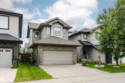 Two-story residential architecture featuring gray siding, stone facade accents, a dark shingle roof, and an attached two-car garage - 115 57 Street, Edmonton, AB 