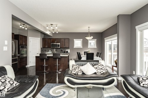 Open-concept living space featuring wood-finish flooring, dark wood cabinetry, stainless steel appliances, and a kitchen island with seating - 115 57 Street, Edmonton, AB 