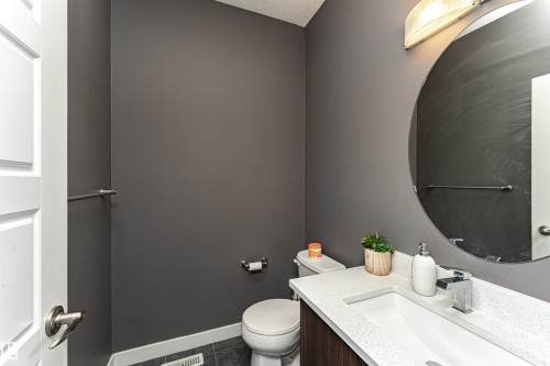 Contemporary powder room featuring dark gray walls, a round mirror, and a vanity with a white speckled countertop and a rectangular undermount sink - 115 57 Street, Edmonton, AB 