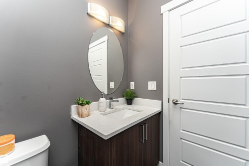 Modern vanity featuring a white solid surface countertop, an undermount sink, and a dark wood-finish cabinet with contemporary hardware - 115 57 Street, Edmonton, AB 