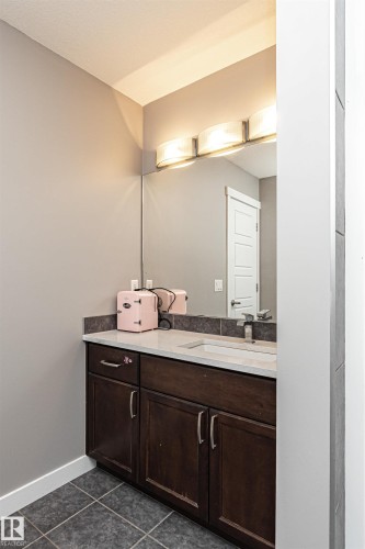 Bathroom vanity featuring dark wood-finish cabinetry, a light-toned countertop with an integrated sink, and a large wall-mounted mirror - 115 57 Street, Edmonton, AB 