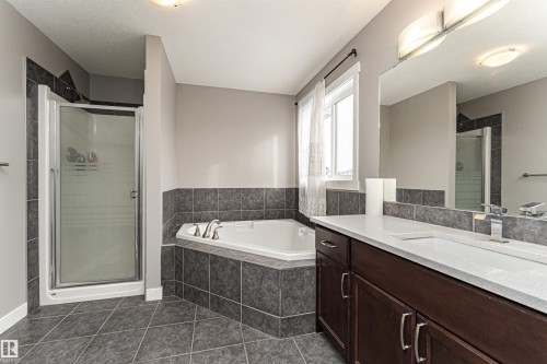 Bathroom featuring a corner soaking tub, a stand-up shower with frosted glass, a dark wood-finish vanity with a single sink, and a large wall-mounted mirror - 115 57 Street, Edmonton, AB 