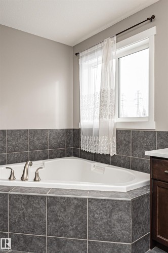 Corner soaking tub with brushed nickel fixtures, surrounded by dark-toned tile - 115 57 Street, Edmonton, AB 