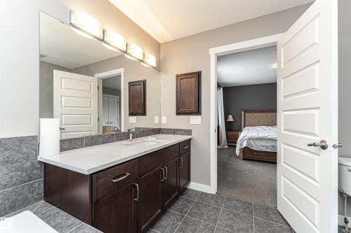 Bathroom vanity featuring a quartz countertop, integrated sink, and dark wood-finish cabinetry with brushed nickel hardware - 115 57 Street, Edmonton, AB 