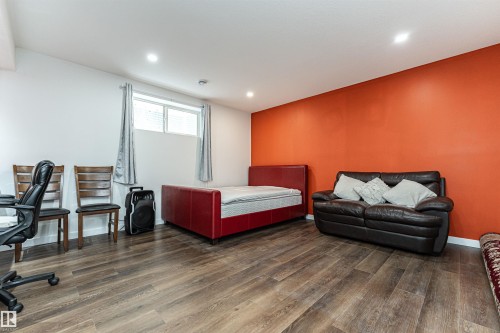 Spacious room featuring wood-finish flooring, a vibrant accent wall, recessed lighting, and a window with blinds - 115 57 Street, Edmonton, AB 