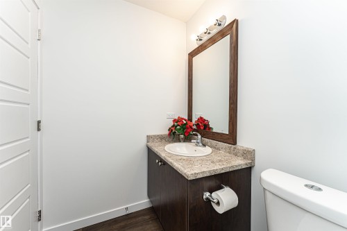 Powder room featuring a dark wood-finish vanity with a stone-finish countertop, undermount sink, and a framed mirror with overhead lighting - 115 57 Street, Edmonton, AB 