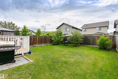Expansive backyard featuring a manicured lawn, wood fencing, mature trees, and a raised wooden deck with white railings - 115 57 Street, Edmonton, AB 