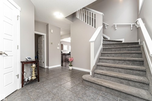 Welcoming entryway featuring large format tile flooring, a carpeted staircase with white railings, and a consistent neutral wall color - 115 57 Street, Edmonton, AB 