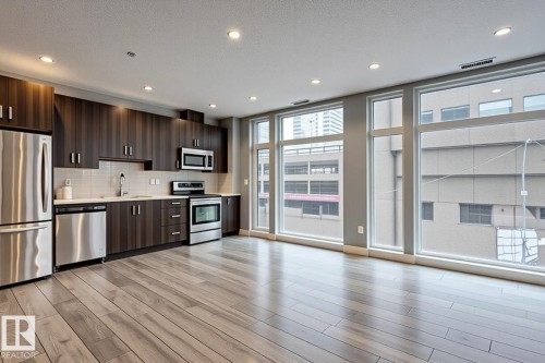 Open-concept kitchen and living area featuring wood-finish flooring, recessed lighting, and expansive windows - 401 10238 103 Street, Edmonton, AB - Indoor Photo Showing Kitchen With Stainless Steel Kitchen With Upgraded Kitchen