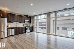 Open-concept kitchen and living area featuring wood-finish flooring, recessed lighting, and expansive windows - 